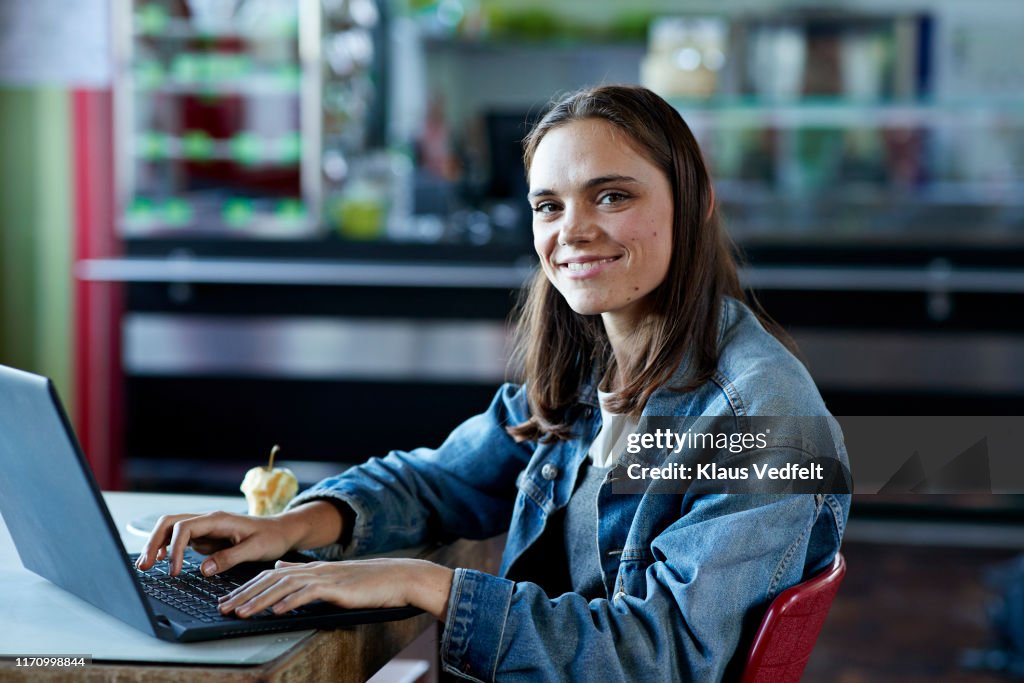 Smiling young female student sitting with laptop
