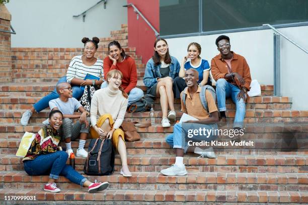 smiling young university students sitting on steps - male student wearing glasses with friends stockfoto's en -beelden