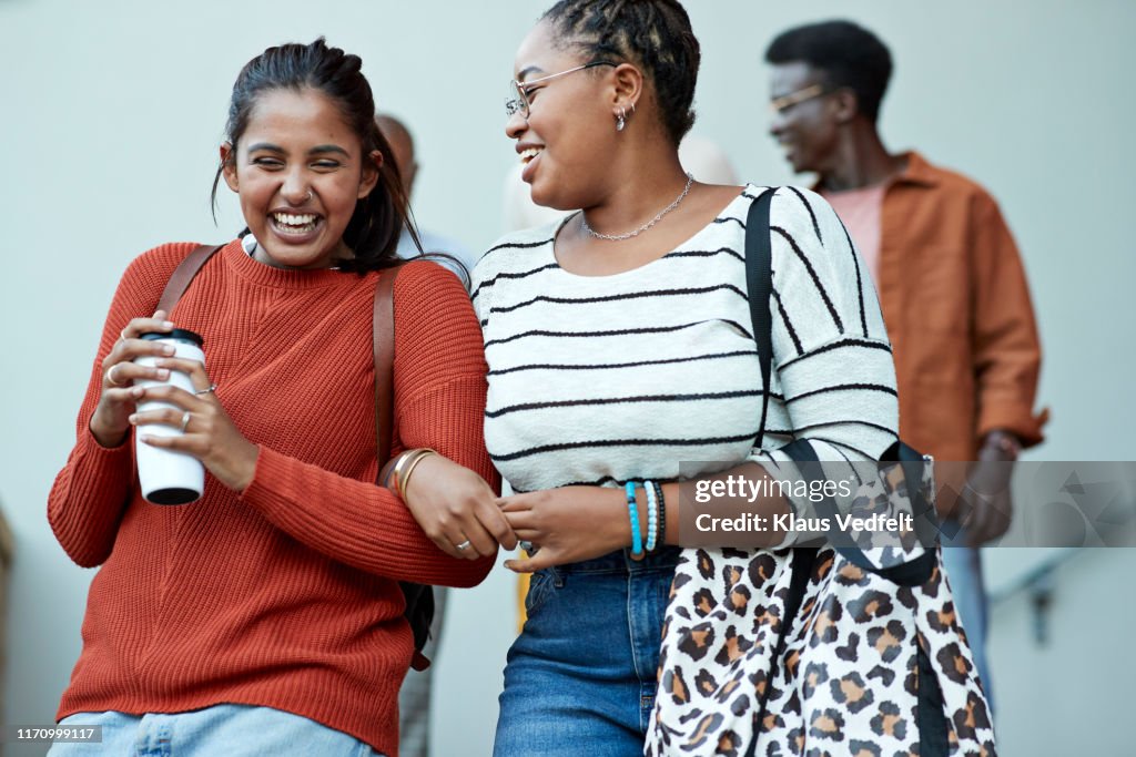 Cheerful friends moving down arm in arm at campus