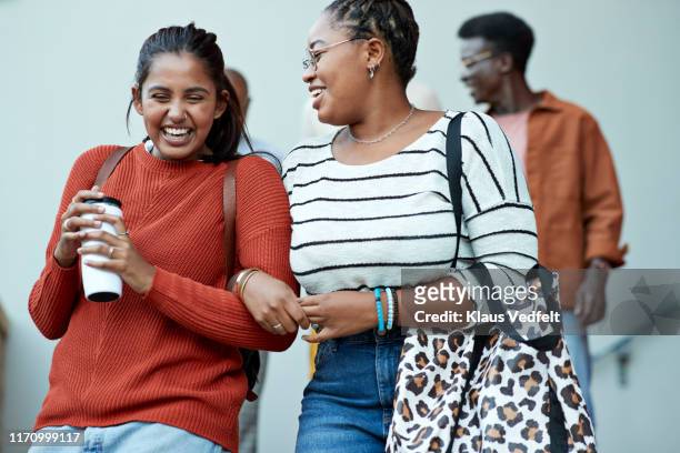 cheerful friends moving down arm in arm at campus - arm in arm stock pictures, royalty-free photos & images