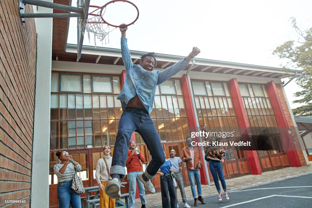 Friends cheering man hanging from basketball hoop