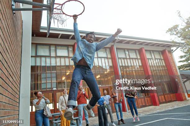 friends cheering man hanging from basketball hoop - womens college basketball stock-fotos und bilder