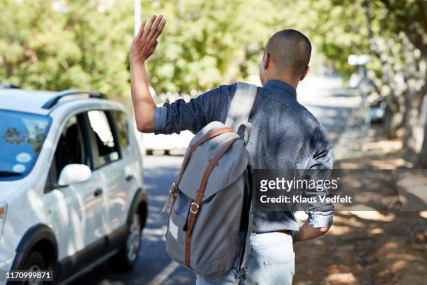 male student waving while waiting on roadside - man waiting foto e immagini stock