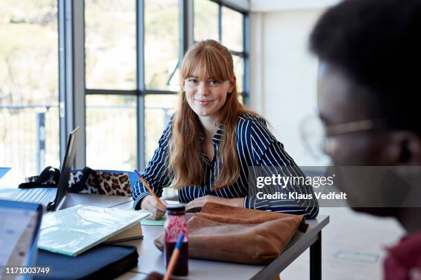 portrait of smiling beautiful young woman at desk - bangs stock-fotos und bilder