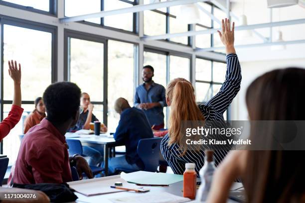 young students raising hands in classroom - pregunta y respuesta fotografías e imágenes de stock