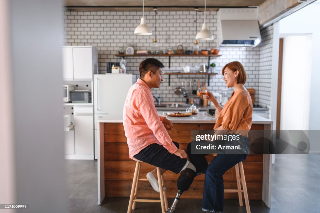 Asian Male Amputee and Wife Relaxing in Kitchen with Tea