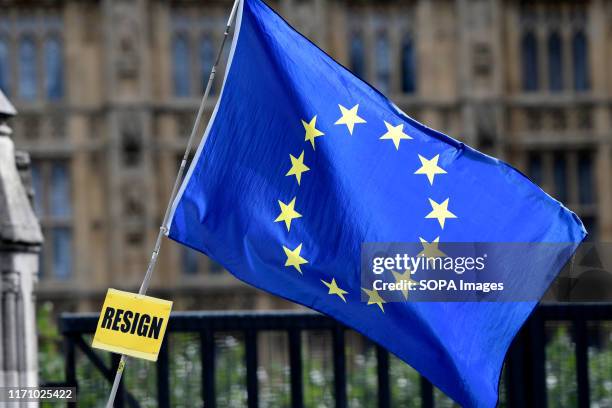 Flag with a sign that says Resign is hangs outside Parliament while UK MPs get back to work.