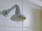Close up of a partly clogged shower head in a bathroom, causing it to putting out so little water