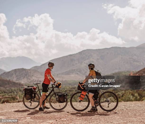 a couple of cyclists look at the view of the atlas mountains, morocco - atlas mountains morocco stock pictures, royalty-free photos & images