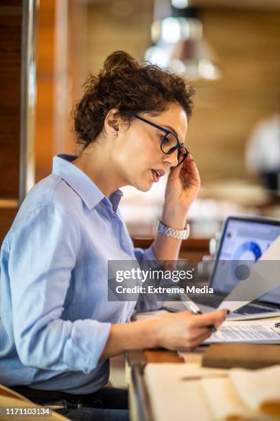 vrouwelijke ondernemer die haar bril vasthoudt en een financiële rapsheet leest terwijl hij in een restaurant zit - stress test stockfoto's en -beelden