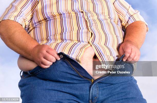 clinically obese man trying to fit into his jeans - bierbauch stock-fotos und bilder