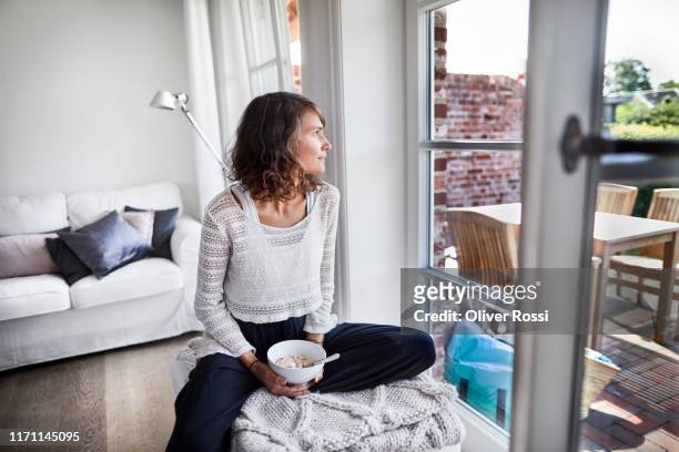 young woman sitting in living room having breakfast - eating alone stockfoto's en -beelden