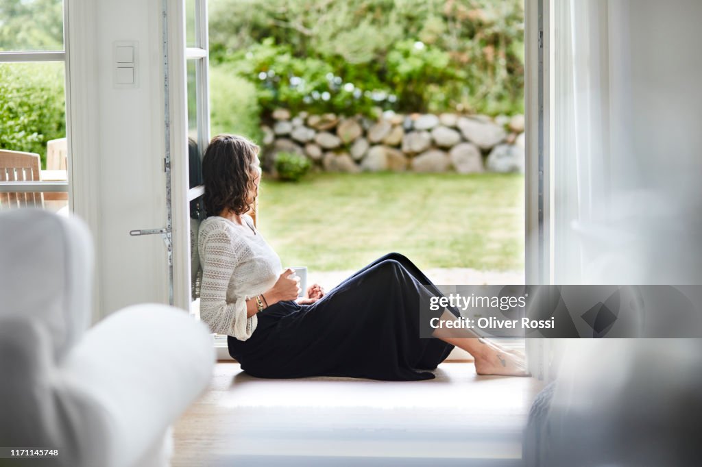 Young woman sitting in windowframe looking out