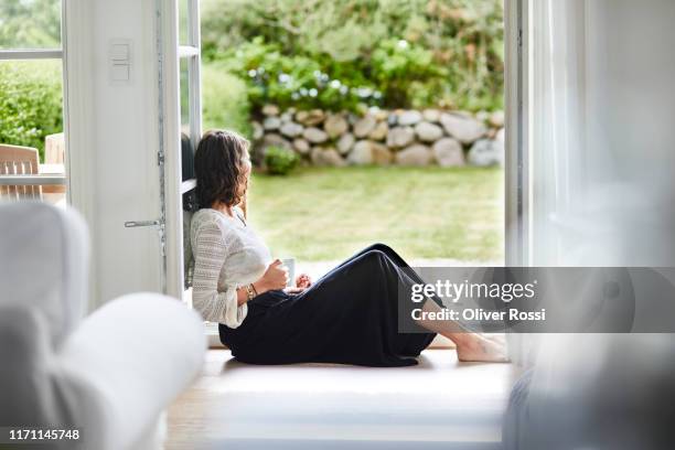 young woman sitting in windowframe looking out - window with view on garden stockfoto's en -beelden