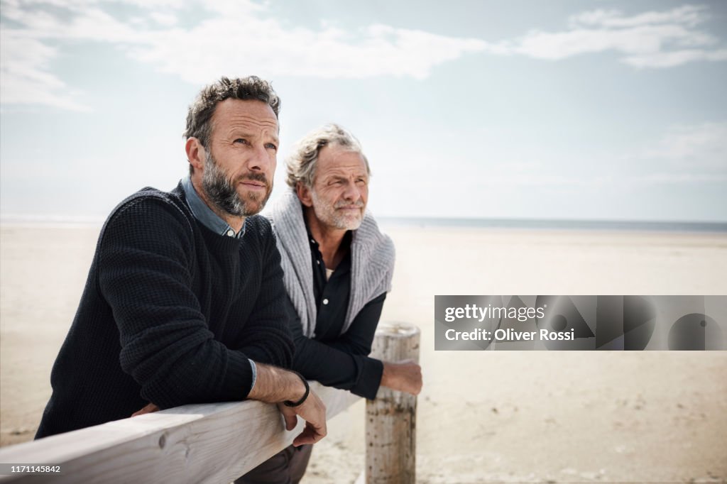 Two mature men leaning on railing of boardwalk on the beach
