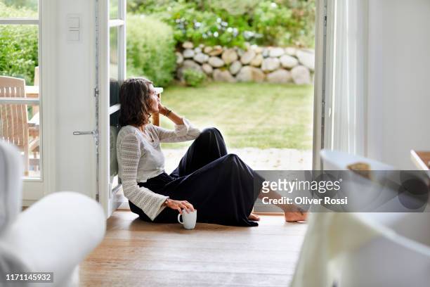 young woman sitting in windowframe looking out - tristeza imagens e fotografias de stock