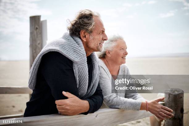 senior couple standing on boardwalk on the beach - 60 woman stockfoto's en -beelden