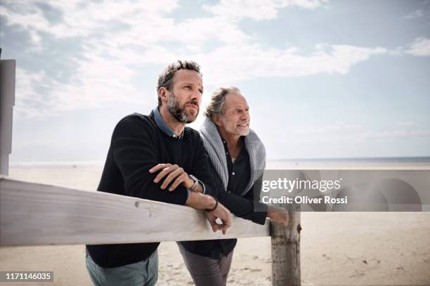 two mature men leaning on railing of boardwalk on the beach - steg zwei menschen stock-fotos und bilder