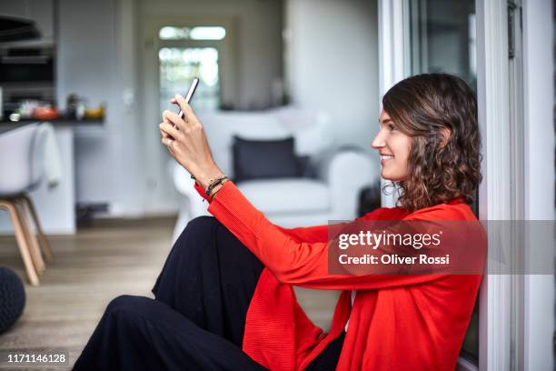 smiling young woman sitting in windowframe using cell phone - red blouse fotografías e imágenes de stock
