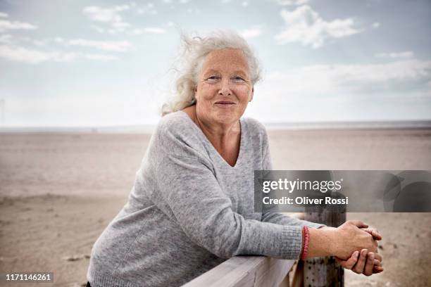 senior woman standing on boardwalk on the beach - tossing hair facing camera woman outdoors stock pictures, royalty-free photos & images