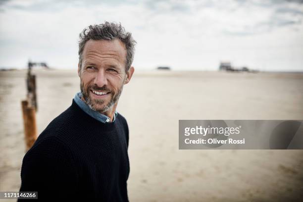 portrait of smiling bearded man on the beach - uomini maturi foto e immagini stock