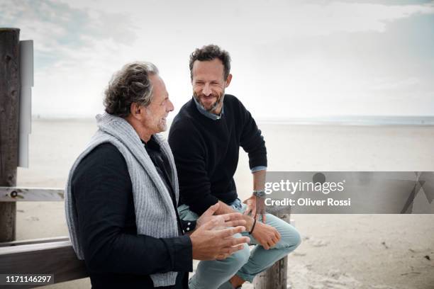 two mature men talking on boardwalk on the beach - friends chatting mature foto e immagini stock