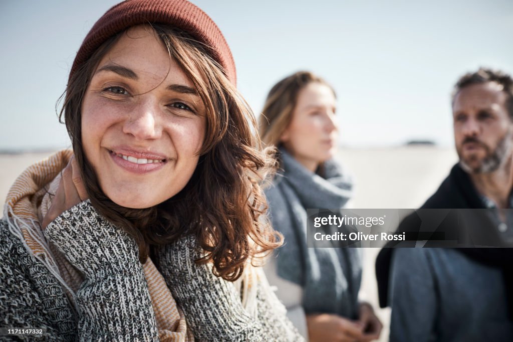 Portrait of smiling young woman on the beach with people in background