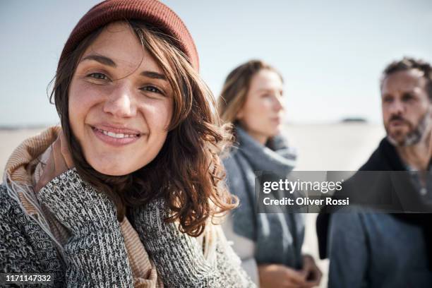 portrait of smiling young woman on the beach with people in background - sea outdoors mature stockfoto's en -beelden