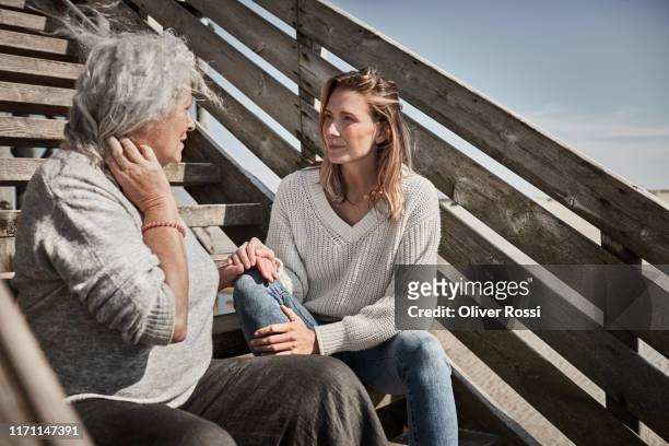 senior woman talking with adult daughter on footbridge at the beach - listening stock-fotos und bilder