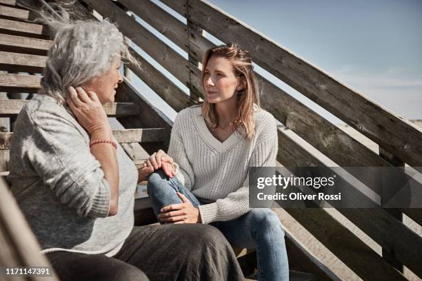 senior woman talking with adult daughter on footbridge at the beach - voetgangersbrug stockfoto's en -beelden