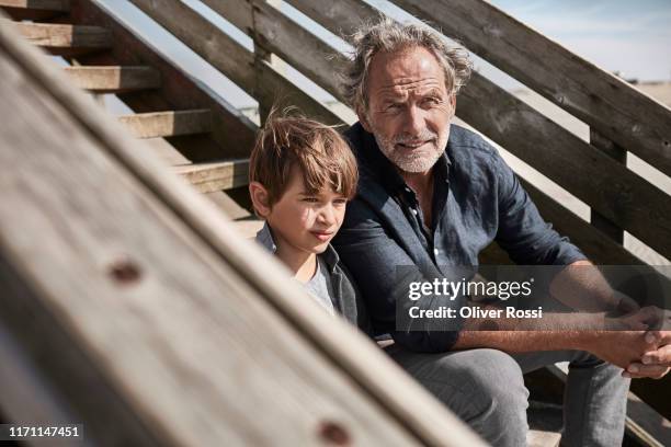 grandfather and gandson sitting on footbridge at the beach - enkelin stock-fotos und bilder