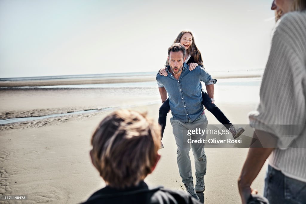 Father carrying daughter piggyback on the beach