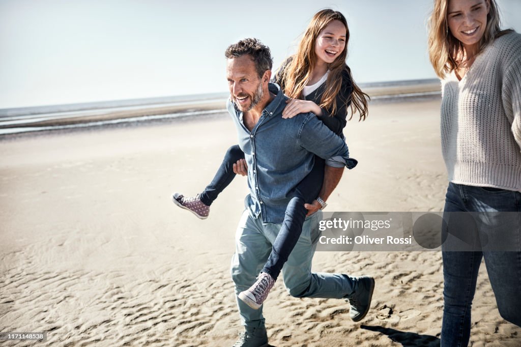 Father carrying daughter piggyback on the beach