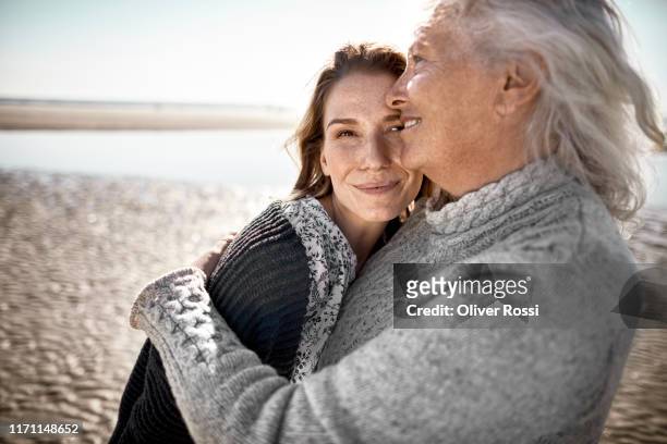 affectionate senior woman with her adult daughter on the beach - family portrait grown up stock-fotos und bilder