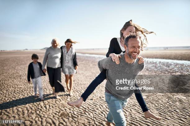 happy father carrying daughter piggyback on the beach - familia en la playa fotografías e imágenes de stock