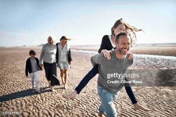 happy father carrying daughter piggyback on the beach - group of mature men stock pictures, royalty-free photos & images