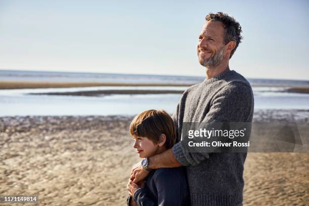 father embracing son on the beach - dad and son stock-fotos und bilder