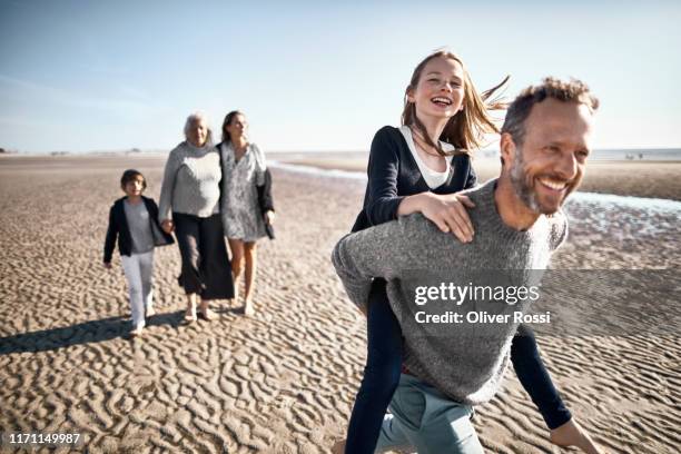 happy father carrying daughter piggyback on the beach - woman child piggyback stock-fotos und bilder