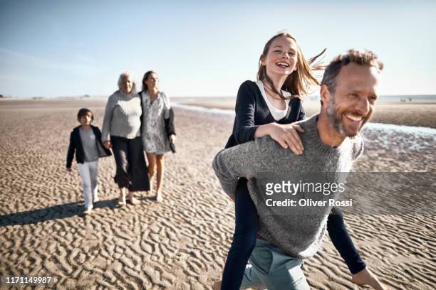 happy father carrying daughter piggyback on the beach - multi generation family walking stock pictures, royalty-free photos & images