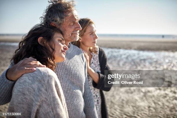 two women and mature man on the beach - contemplation family stock-fotos und bilder