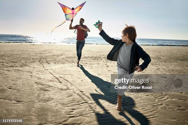 father and son flying kite on the beach - children kite stock pictures, royalty-free photos & images