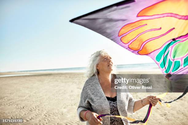 senior woman with kite on the beach - kite toy stock-fotos und bilder