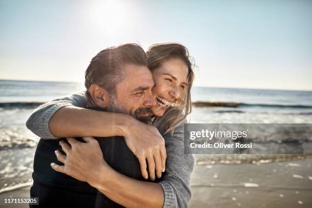 carefree mature man and woman hugging at the sea - frau zwischen 50 und 60 stock-fotos und bilder