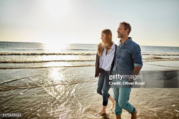 man and young woman wading in the sea - beach walking stock-fotos und bilder