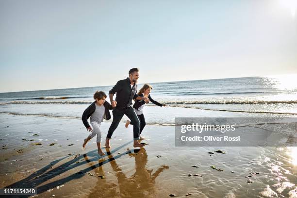 father with two children running at the sea - german north sea region stock pictures, royalty-free photos & images