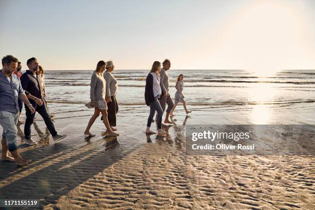 family strolling on the beach at sunset - ballade famille photos et images de collection