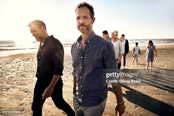 two men with family strolling on the beach at sunset - atividade imóvel imagens e fotografias de stock