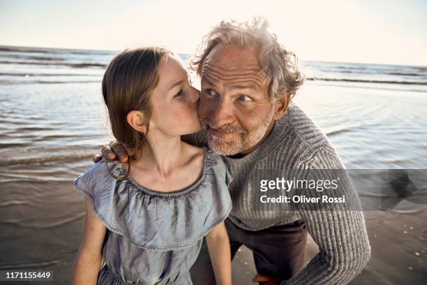 granddaughter kissing her grandfather on the beach - granddaughter stock pictures, royalty-free photos & images
