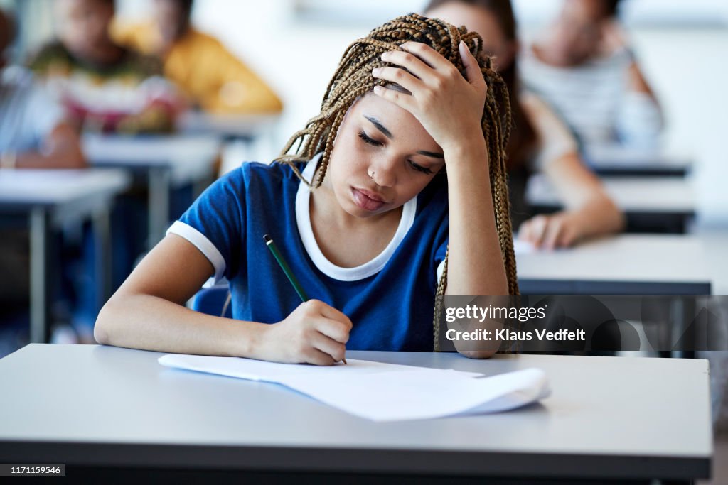 Young braided hair woman writing exam at desk