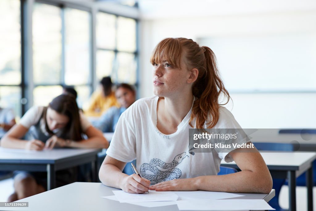 Thoughtful student looking away while writing exam